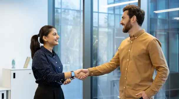 Eine Frau und ein Mann schütteln sich die Hand zur Begrüßung in einem Büro.